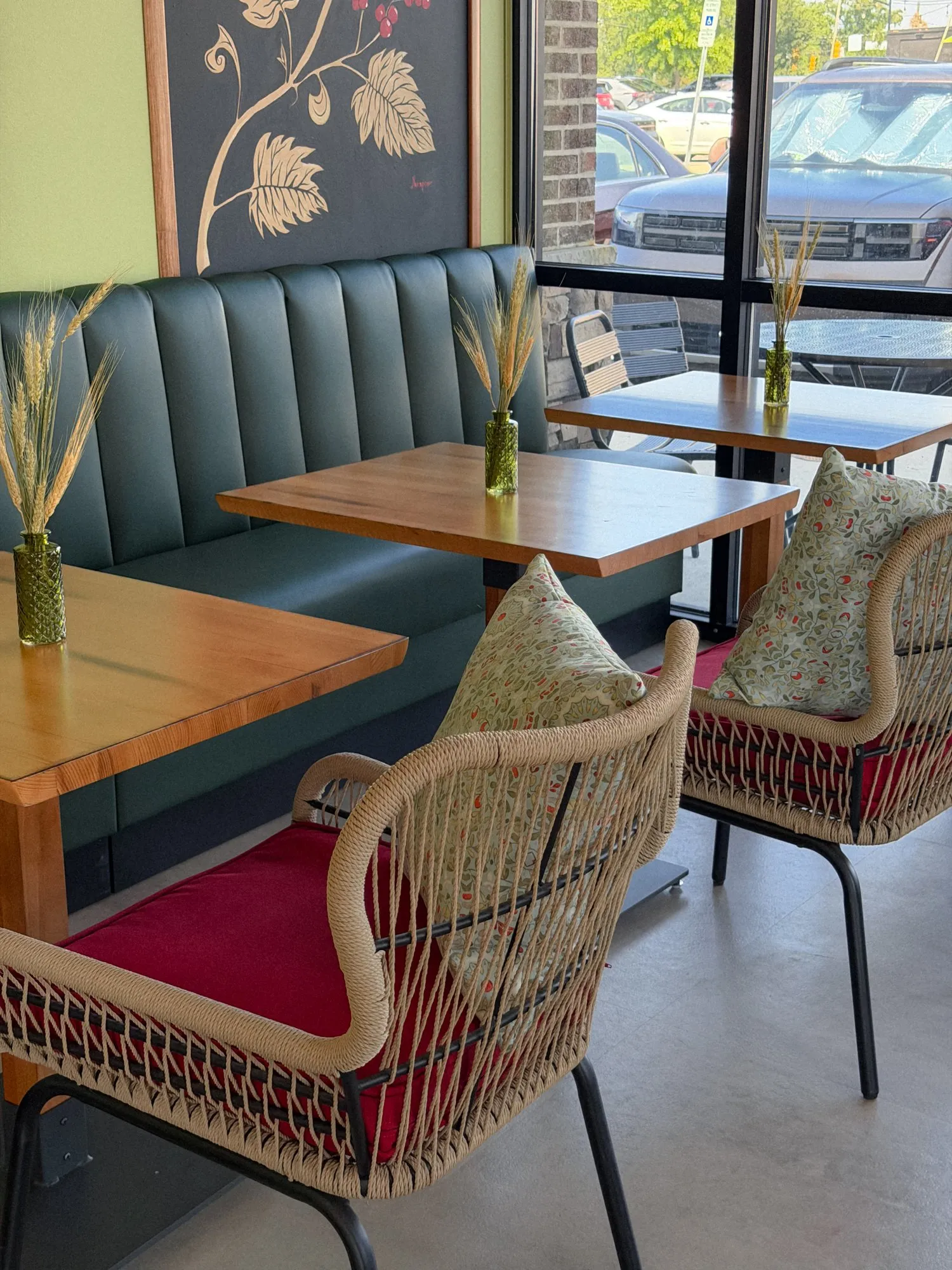 Wooden tables along the teal banquette, each with a vase of wheat