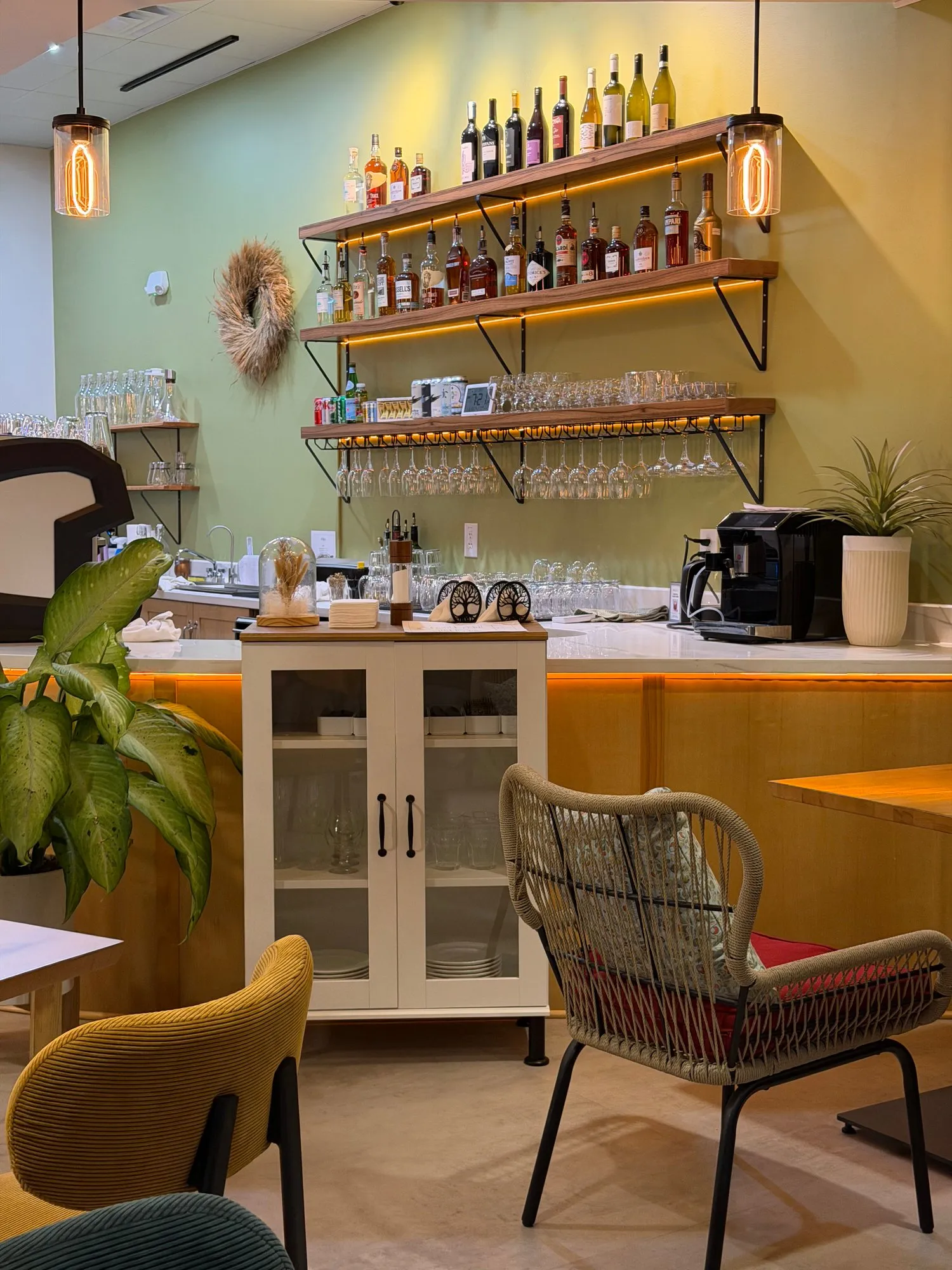 Rattan and velvet chairs in front of the bar and its lit wine shelves
