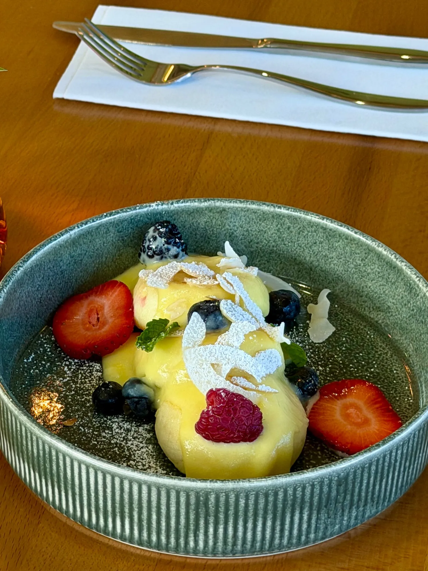 Syrnyki under vanilla sauce with strawberries, blueberries and coconut