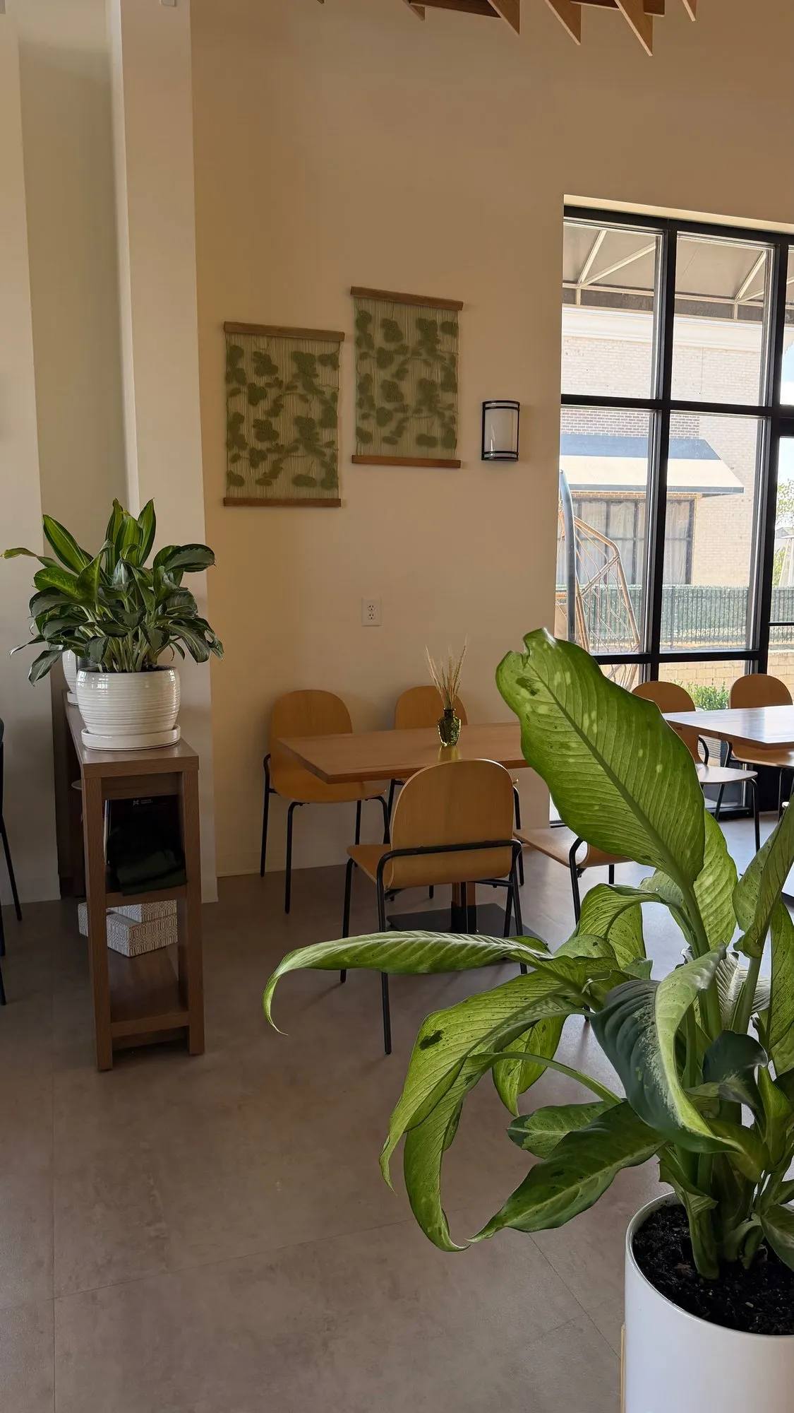 Botanical wall hangings above tables on the daylit side of the dining room